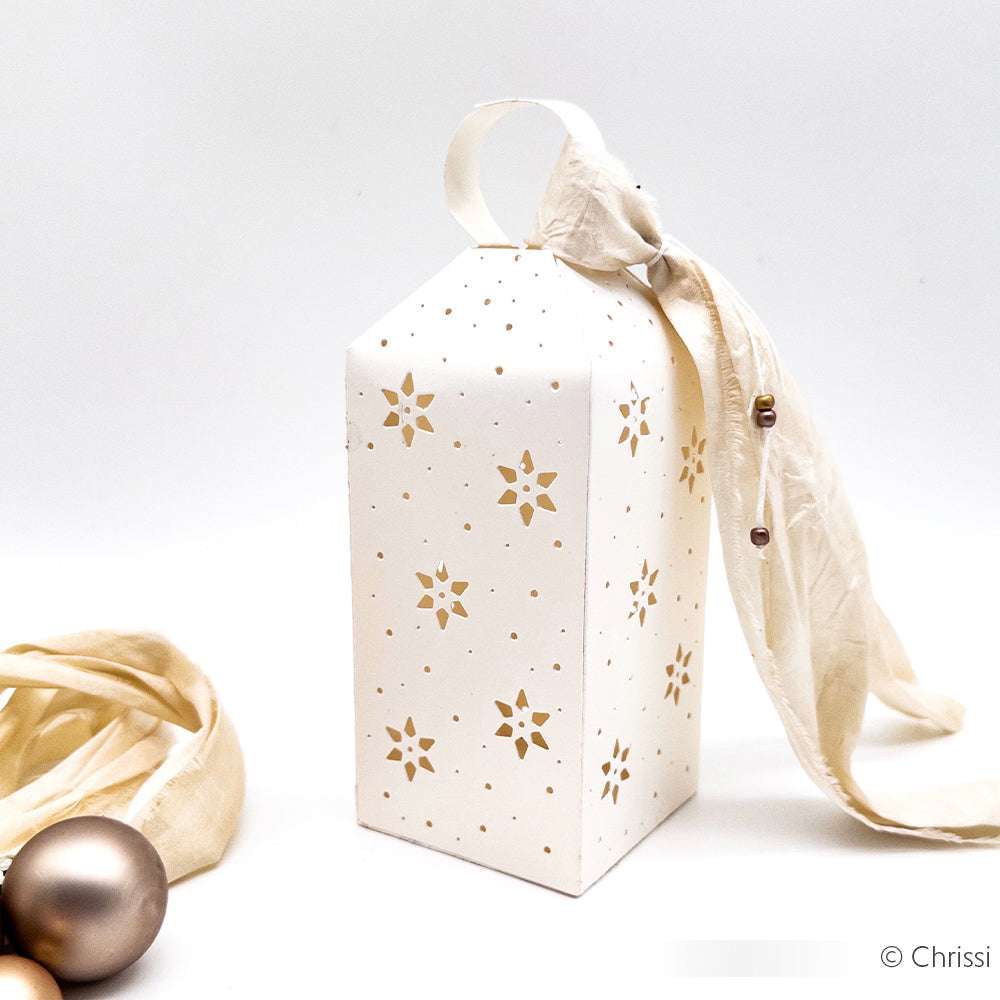 Hohe weiße Geschenkschachtel mit goldenen Sternmustern, Bandhenkel und elfenbeinfarbenem Stoff neben goldenen Ornamenten - hergestellt mit Alexandra Renke PAPPcut Deep Edge Motivstanzen für einen raffinierten Touch.