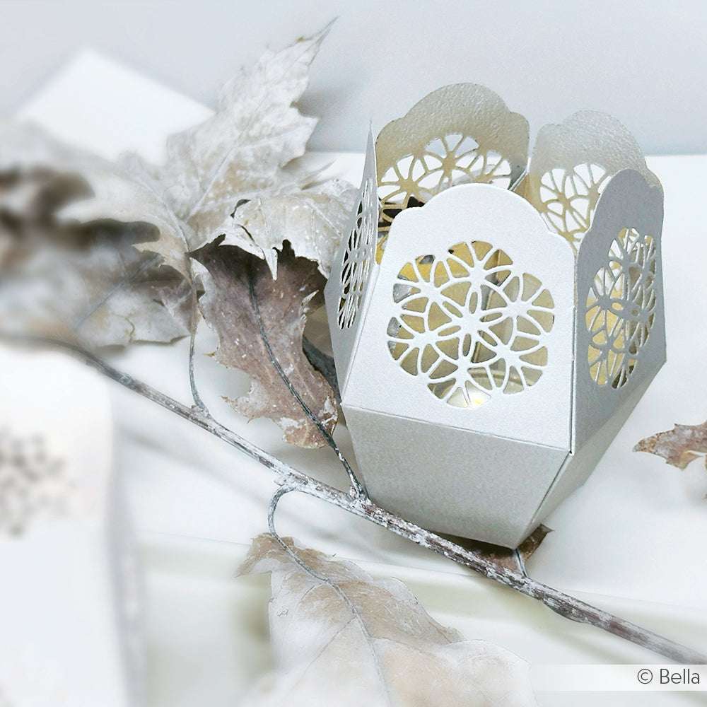 Dekoratives weißes Papierwindlicht von Alexandra Renke, gefertigt mit der Motivstanze Windlicht Ornament und mit kunstvollen Ausschnitten neben gefrosteten Blättern und Zweigen.