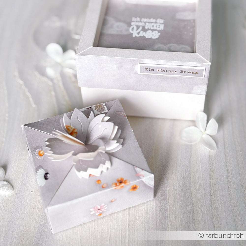 Zwei dekorative pastellfarbene Geschenkboxen mit floralen Motiven und deutschen Etiketten, gefertigt mit der Motivstanze Prunkblüten Box von Alexandra Renke, stehen auf einer hellen Fläche.