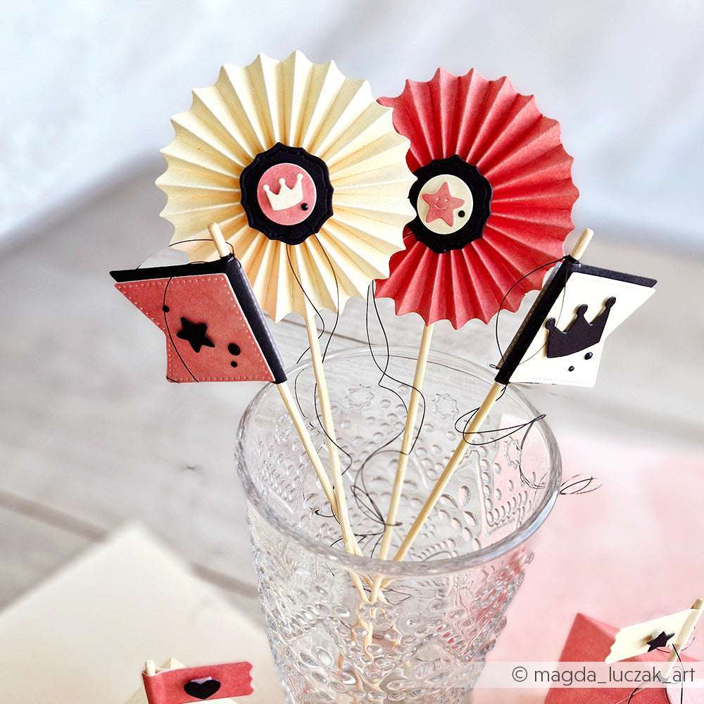 Papierdekorationen, die mit Alexandra Renke Deep Edge Motivstanzen und PAPPcut®ies - Kronen und Sterne auf Holzstäben - hergestellt wurden, werden in einer strukturierten Glastasse auf einem hellen Tisch präsentiert.