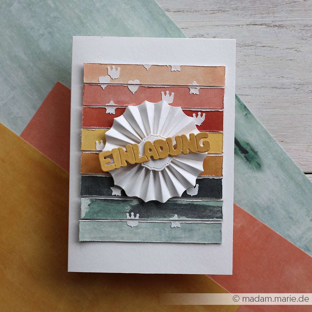Handgemachte Karte von Alexandra Renke mit farbigen Streifen und "EINLADUNG" auf einer weißen Rosette, hergestellt mit Designpapieren und einer Motivstanze Rosette, dargestellt auf bunten Papieren.