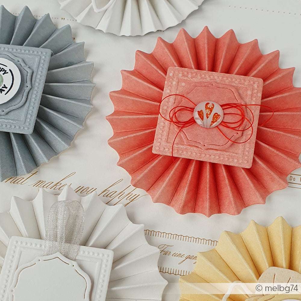 Pastellfarbene Papierrosetten mit dekorativen quadratischen Zentren, hergestellt mit Alexandra Renke Motivstanze Rosette und PAPPcut®ies, angeordnet auf einem hellen Hintergrund.