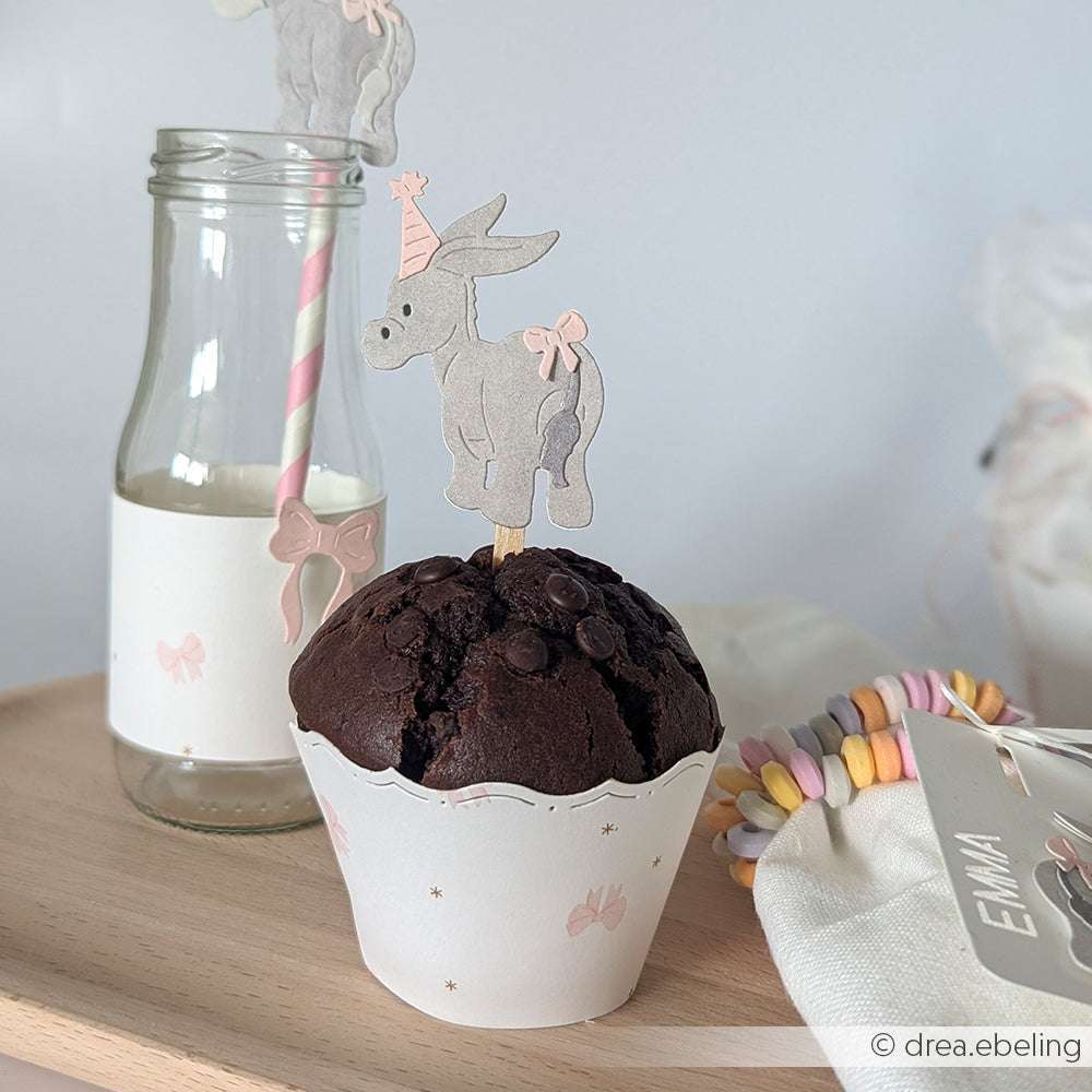 Schokoladenmuffin mit einem Alexandra Renke PAPPcut®ies Esel als Topper, daneben eine Milchflasche mit rosa Strohhalm auf einem Holztablett - dekoriert mit einer entzückenden Alexandra Renke Muffin-Banderole für zusätzlichen Charme.