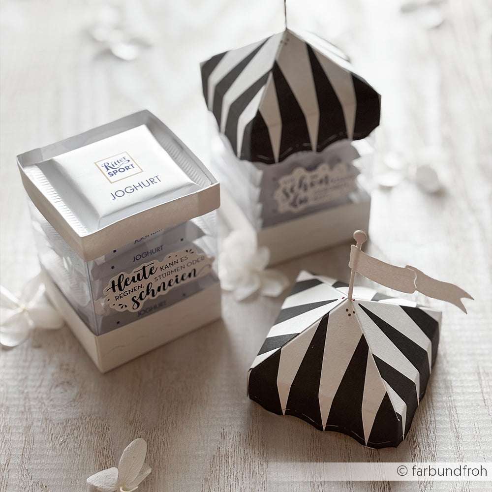 Ein Joghurtbecher mit zwei schwarz-weiß gestreiften Alexandra Renke PAPPcut®ies Motivstanze Festliche Zelt Box Geschenkboxen auf einer hellen Holzoberfläche.
