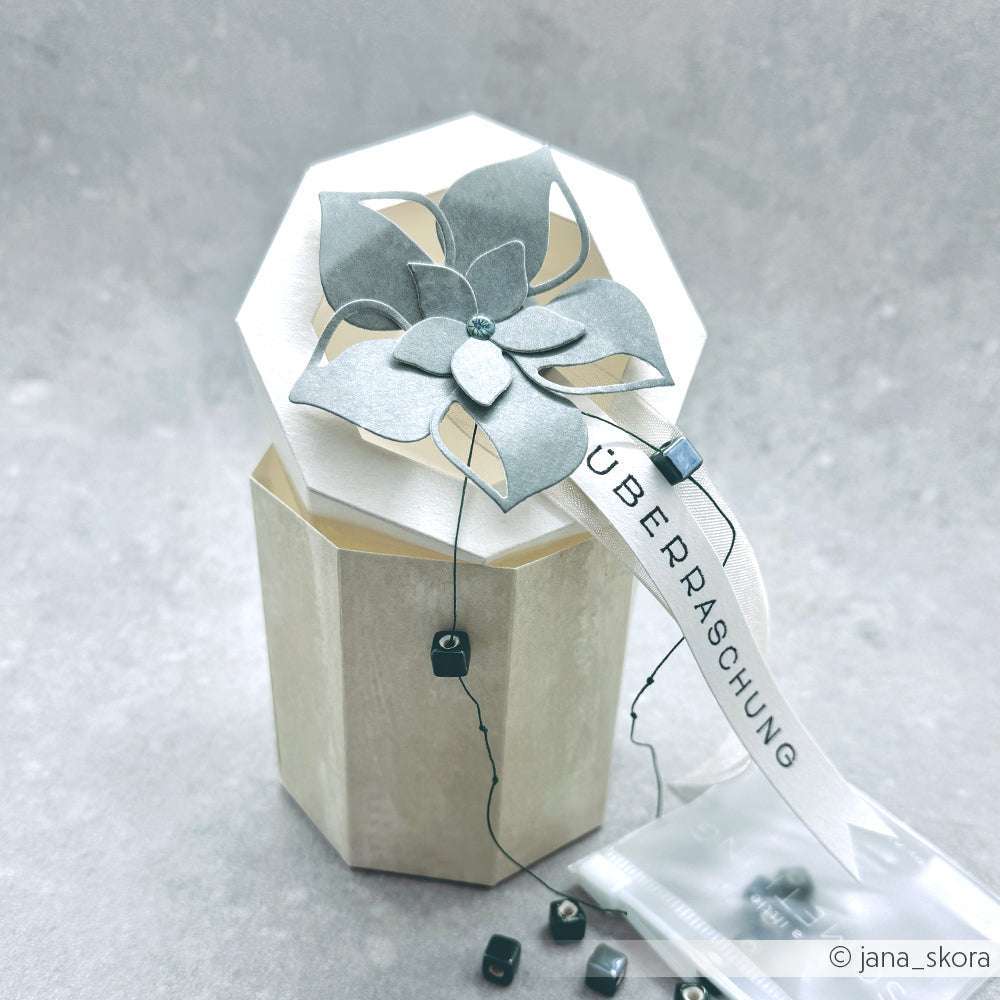 Achteckige Geschenkschachtel von Alexandra Renke, hergestellt mit PAPPcut®ies und gekrönt mit einer Papierblume, mit einem "Überraschung"-Anhänger. Fachmännisch geformt mit Deep Edge Stanzen für scharfe Kanten und komplizierte Details.