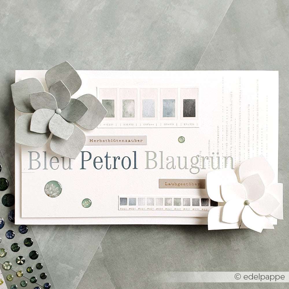 Handgefertigte Karte mit Papierblumen aus Alexandra Renke Deep Edge Motivstanzen und der Motivstanze Faltzauber-Blume, Farbmustern und Bleu Petrol Blaugrun Schriftzug auf grauem Hintergrund.