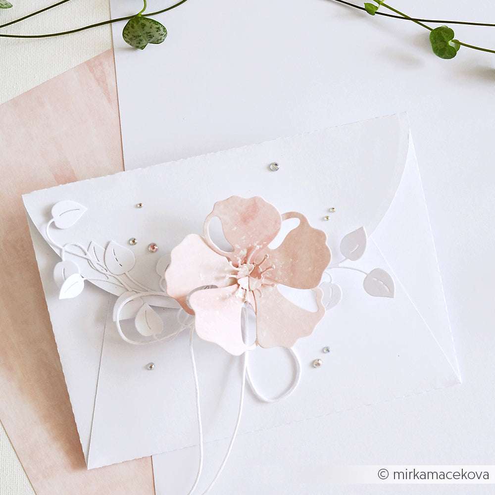 Ein weißer Umschlag, verziert mit einer rosafarbenen Papierblume, Blattdetails und Perlen - elegant gestaltet mit der Motivstanze Faltzauber-Mohn von Alexandra Renke.