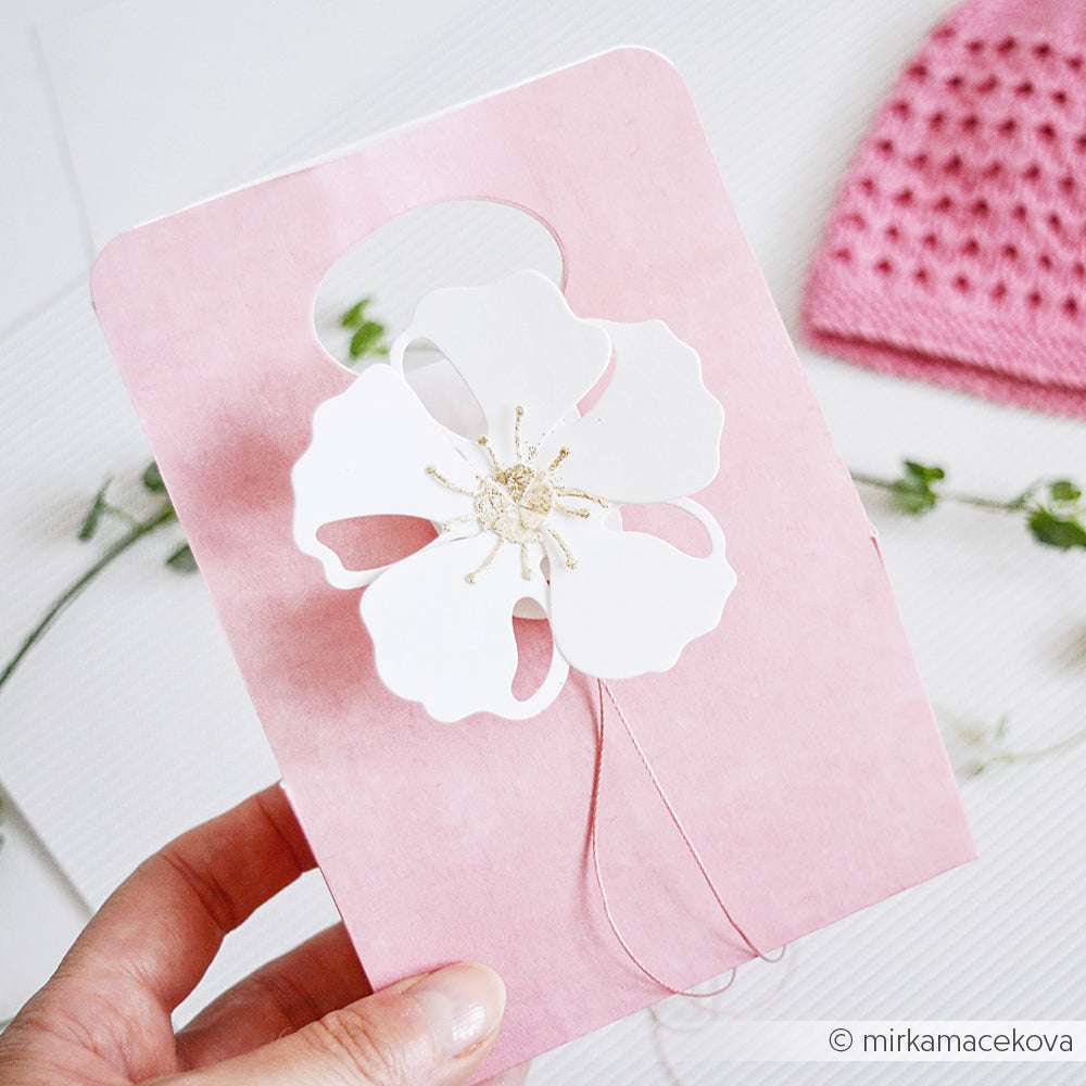 Eine Hand hält eine rosafarbene Karte mit einem großen weißen Blumenausschnitt und gestickten Details, die mit Alexandra Renke Deep Edge Stanzen für ein präzises Design gefertigt wurden.