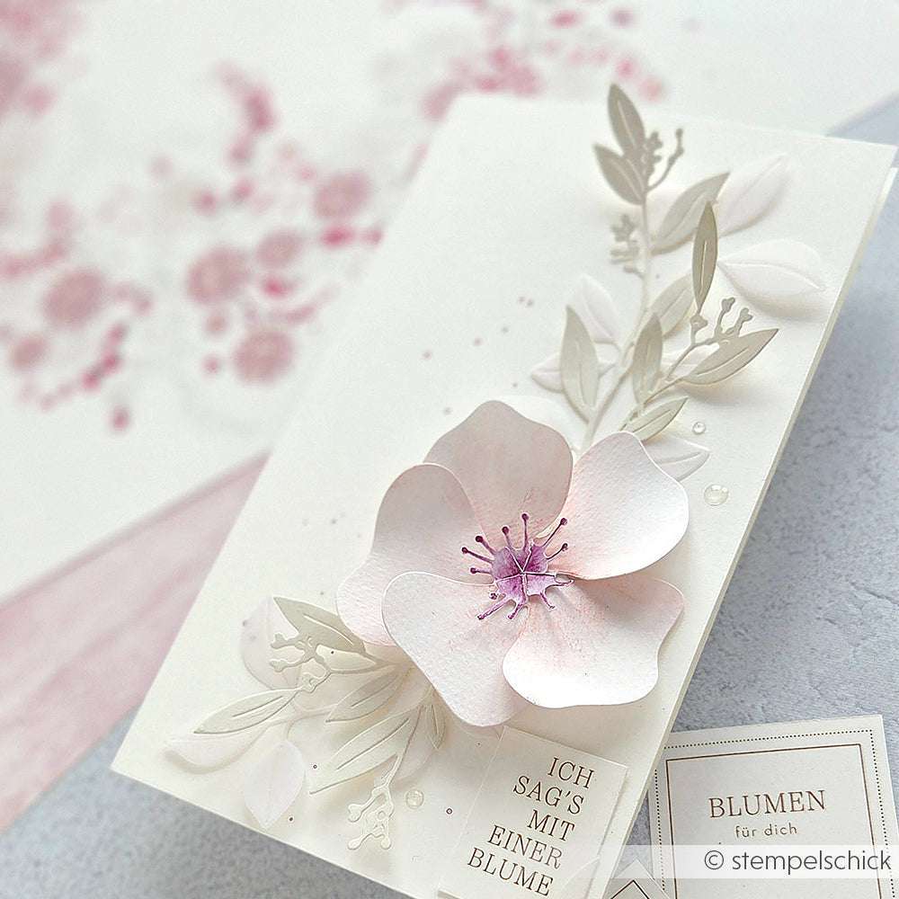 Eine handgefertigte Alexandra Renke PAPPcut®ies Karte mit einer pastellfarbenen 3D-Blume, zarten Blättern und deutschem Text, erstellt mit Deep Edge Motivstanzen auf einem hellen Hintergrund.