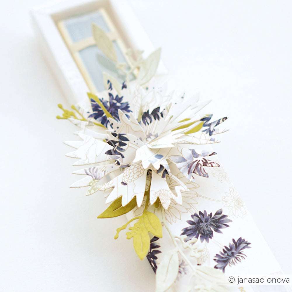 Weiße Geschenkschachtel mit geschichteten PAPPcut®ies-Papierblumen und -blättern in sanften Weiß-, Grün- und Violetttönen von Alexandra Renke, die mit Deep Edge Motivstanzen für einen zarten, eleganten Touch verarbeitet wurden.