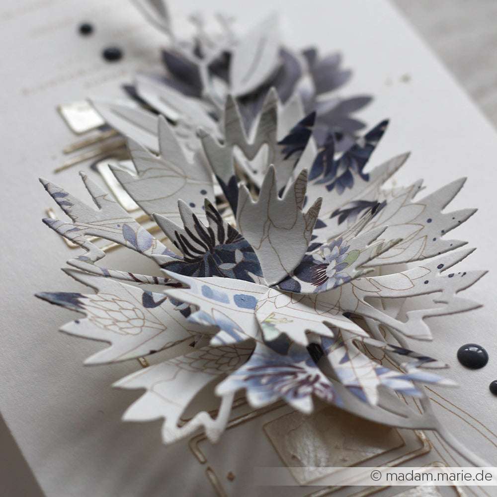 Eine Nahaufnahme eines handgemachten 3D-Papierblumenmusters mit geschichteten Blättern und blauen Blumenmustern, hergestellt mit Alexandra Renke Deep Edge Motivstanzen und Motivstanze Faltzauber-Kornblume.