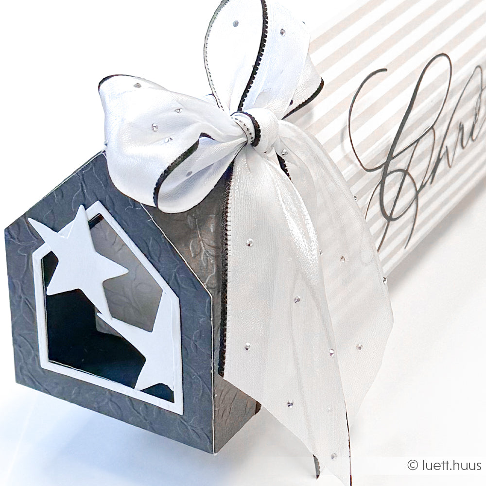 Alexandra Renke Geschenkbox in Form eines Hauses mit Sternausschnitt, hergestellt mit DieCut Systemen, eingewickelt in gestreifte Designpapiere und mit einem weißen Band verschnürt.