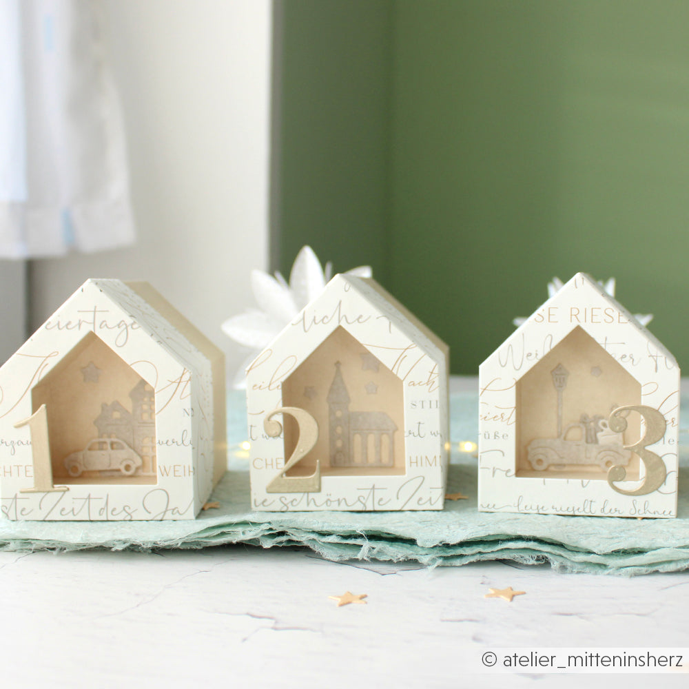 Die drei dekorativen Papierhäuser mit den Nummern 1, 2 und 3 sind im Inneren mit ausgeschnittenen Auto- und Gebäudedesigns versehen - hergestellt mit Alexandra Renke Stanzsystemen und Motivstanze Haus Box für präzise Details.