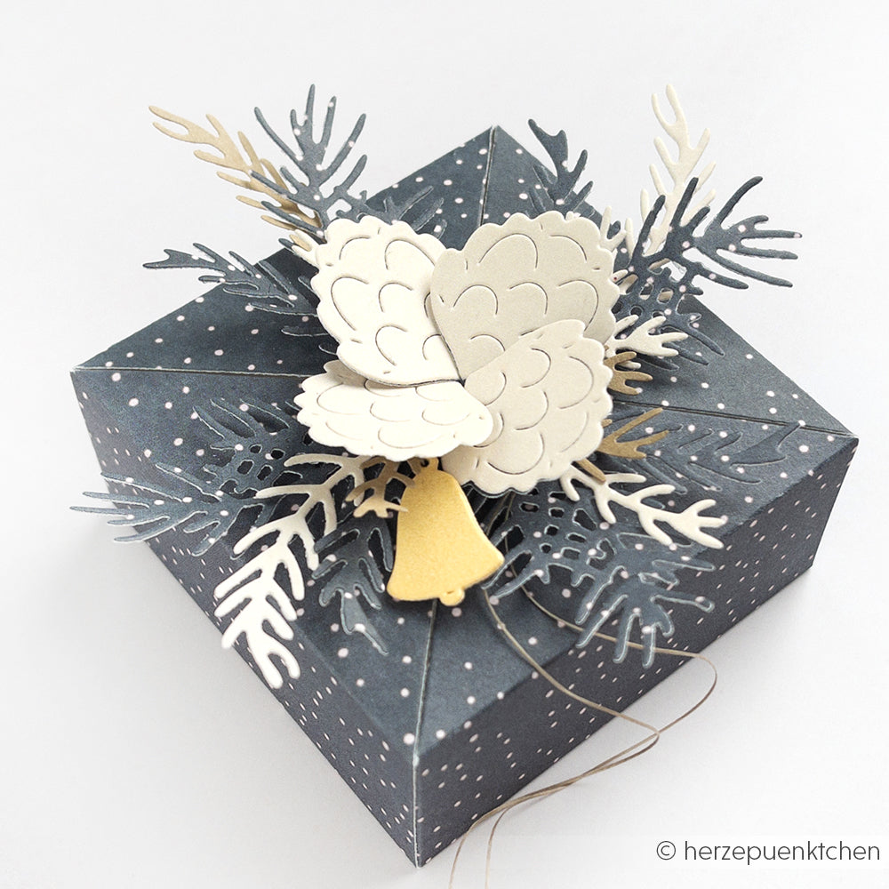 Dunkelblaue Geschenkschachtel mit weißen Punkten, dekoriert mit Alexandra Renke Designpapiere und Motivstanze Tannenzweig für die Tannenzapfen und -zweige aus Papier sowie einer kleinen goldenen Glocke.