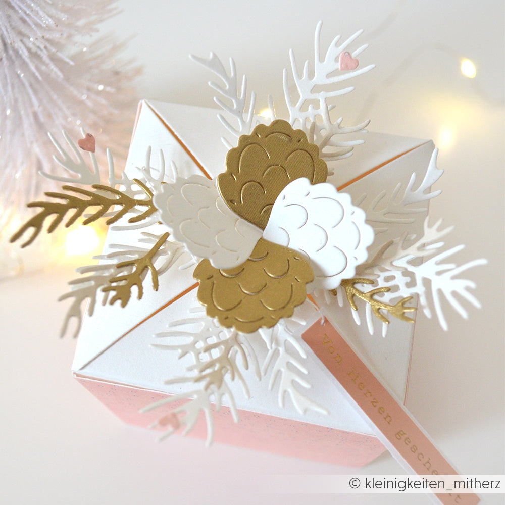 Geschenkkarton von Alexandra Renke mit goldenen und weißen Tannenzapfen aus Papier, weißen Blättern aus einer Motivstanze und einem rosa Anhänger mit der Aufschrift "Von Herzen Geschenk".