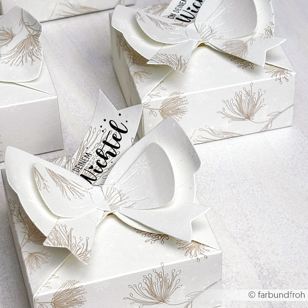 Die weißen Geschenkboxen von Alexandra Renke sind mit floralen Mustern, großen Papierschleifen und Wichtelanhängern versehen - gefertigt mit der Motivstanze Schleifenbox und eleganten Designpapieren für eine charmante Präsentation.