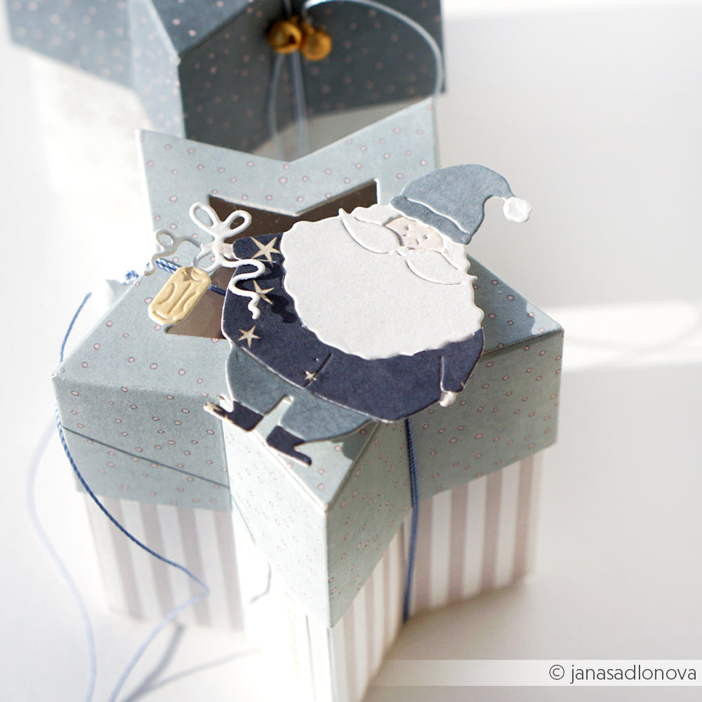 Sternförmige Geschenkbox aus der Alexandra Renke Motivstanze Stern-Box, gekrönt mit einem blau-weißen Weihnachtsmann-Dekor und verschnürt mit einer Schnur.