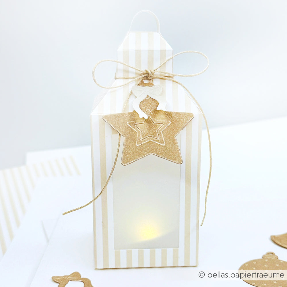 Weiß und gold gestreifte Geschenkbox im Laternenstil von Alexandra Renke mit Sternanhänger, Schleife, Designpapieren und einem sanft leuchtenden Licht im Inneren.