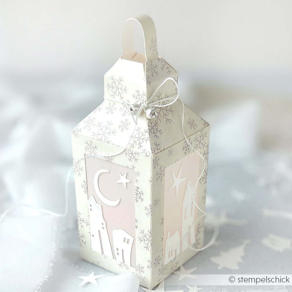 Weiße Papierlaternen-Geschenkbox von Alexandra Renke, gefertigt mit der Motivstanze Laternen Box, mit Winterdorf, Mond und Sternen zum Ausschneiden, verziert mit einer silbernen Schleife.