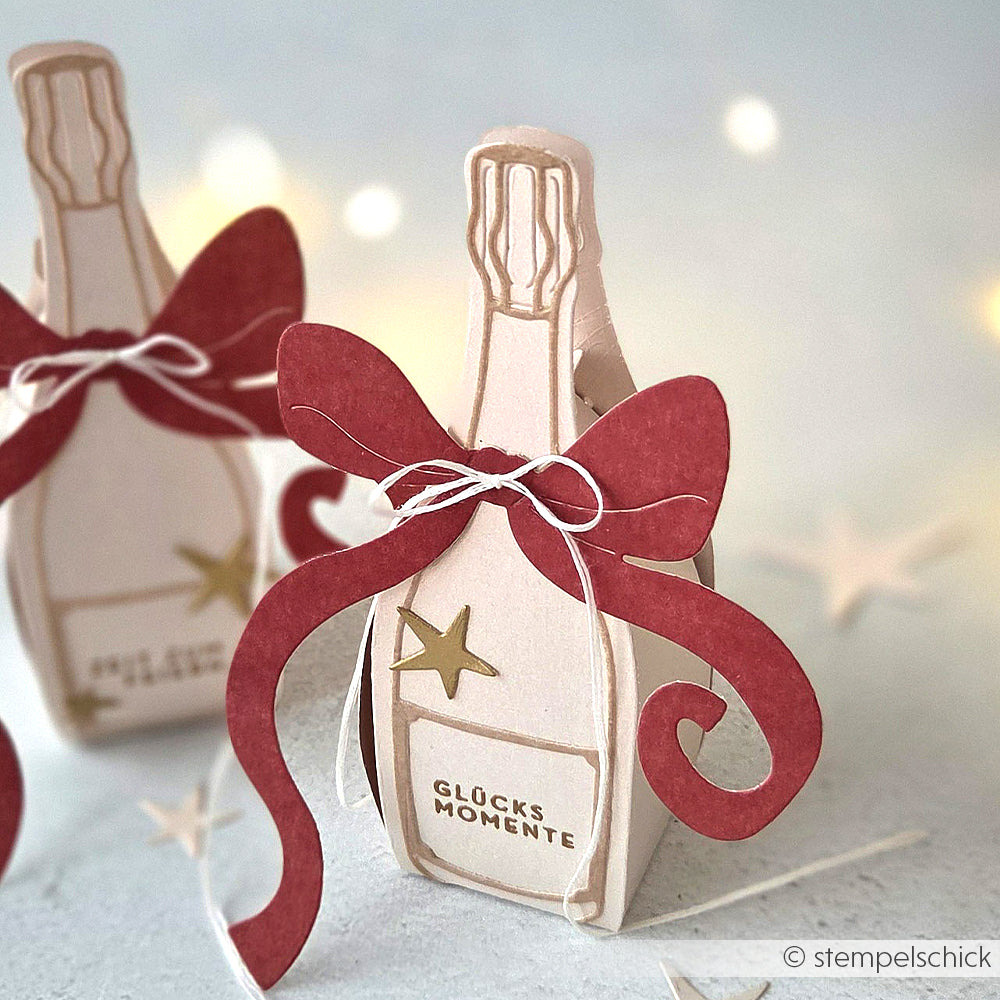 Eine Sektflaschen-Geschenkbox aus Papier von Alexandra Renke, hergestellt mit Designpapieren, mit roter Schleife, goldenem Stern und Glücksmomente-Etikett - perfekt geformt mit der Motivstanze Champagner Box.