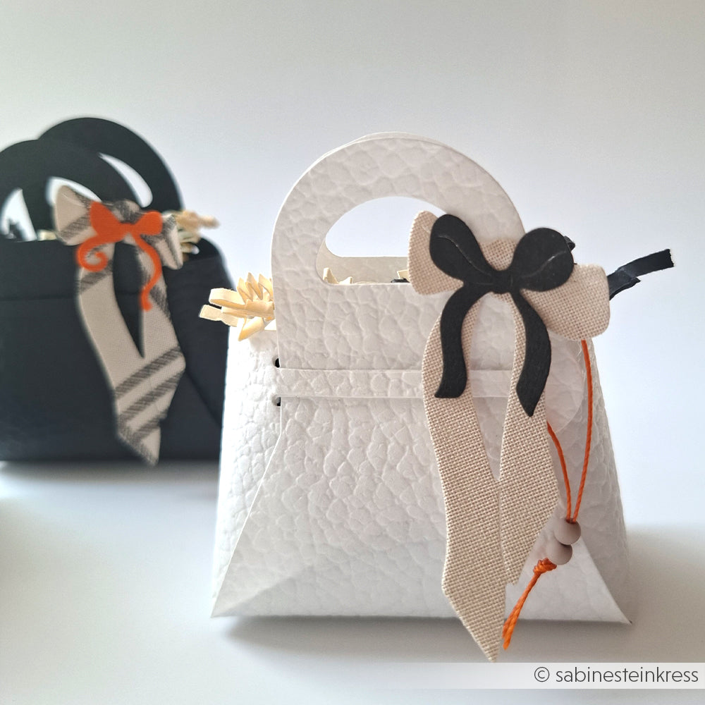 Zwei kleine, strukturierte Geschenktaschen von Alexandra Renke aus eleganten Designpapieren, mit Henkeln und Schleife - eine vorne weiß, eine hinten schwarz. Ideal zum Präsentieren von Kreationen aus der Motivstanze Steck-Tasche oder anderen Stanzsystemen.