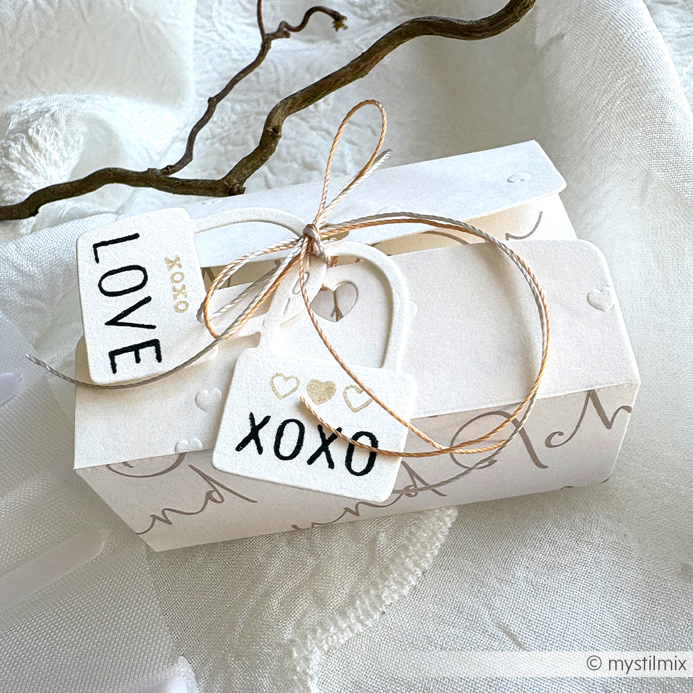 Weiße Geschenkbox von Alexandra Renke mit Schleife aus Garn, herzförmigem Anhänger aus Motivstanzen und LOVE/XOXO-Karten auf Spitzenstoff.