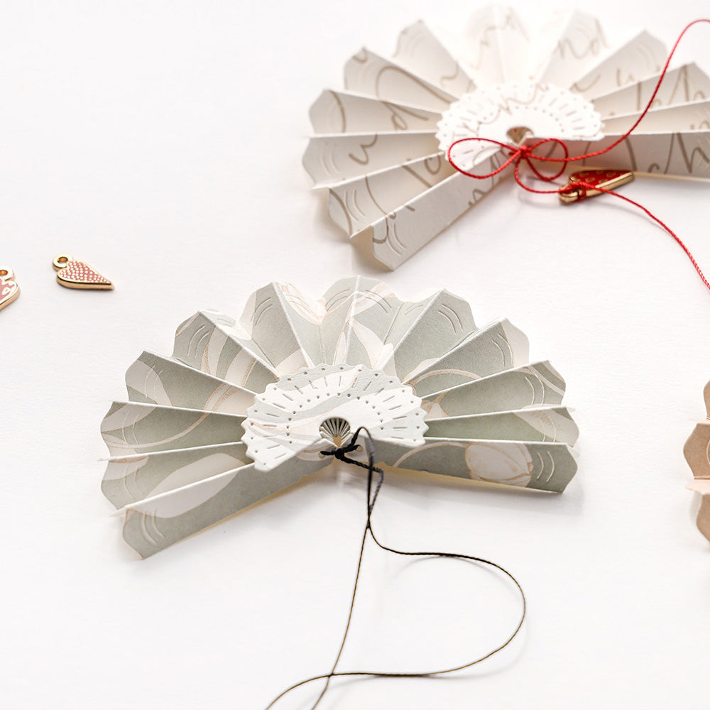 Die akkordeongefalteten Papierfächer von Alexandra Renke aus Designpapier mit schwarzen und roten Fäden zeigen zarte Muster auf weißer Oberfläche. Perfekt für kreative Projekte mit Motivstanze Faltfächer klein oder DieCut Systeme.