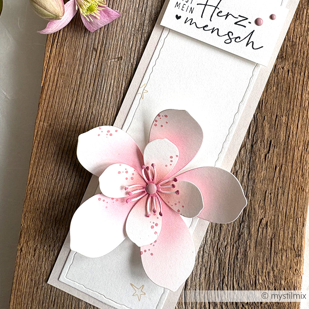 Eine handgefertigte Karte von Alexandra Renke mit einer großen rosafarbenen und weißen Papierblume, die mit Designpapieren und der Motivstanze 3D Kirschblüte gestaltet wurde, sowie einem "Herz mensch"-Anhänger am oberen Rand.
