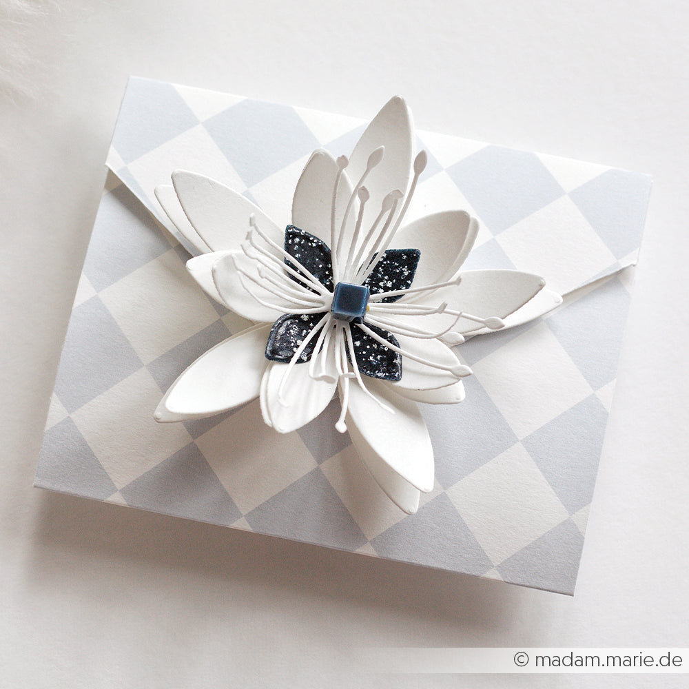 Briefumschlag mit geometrischem Muster, gestaltet mit Alexandra Renke Designpapieren und verziert mit einer geschichteten weißen und schwarzen Blume, die mit dem Motivstanze 3D Sternblume DieCut System hergestellt wurde.