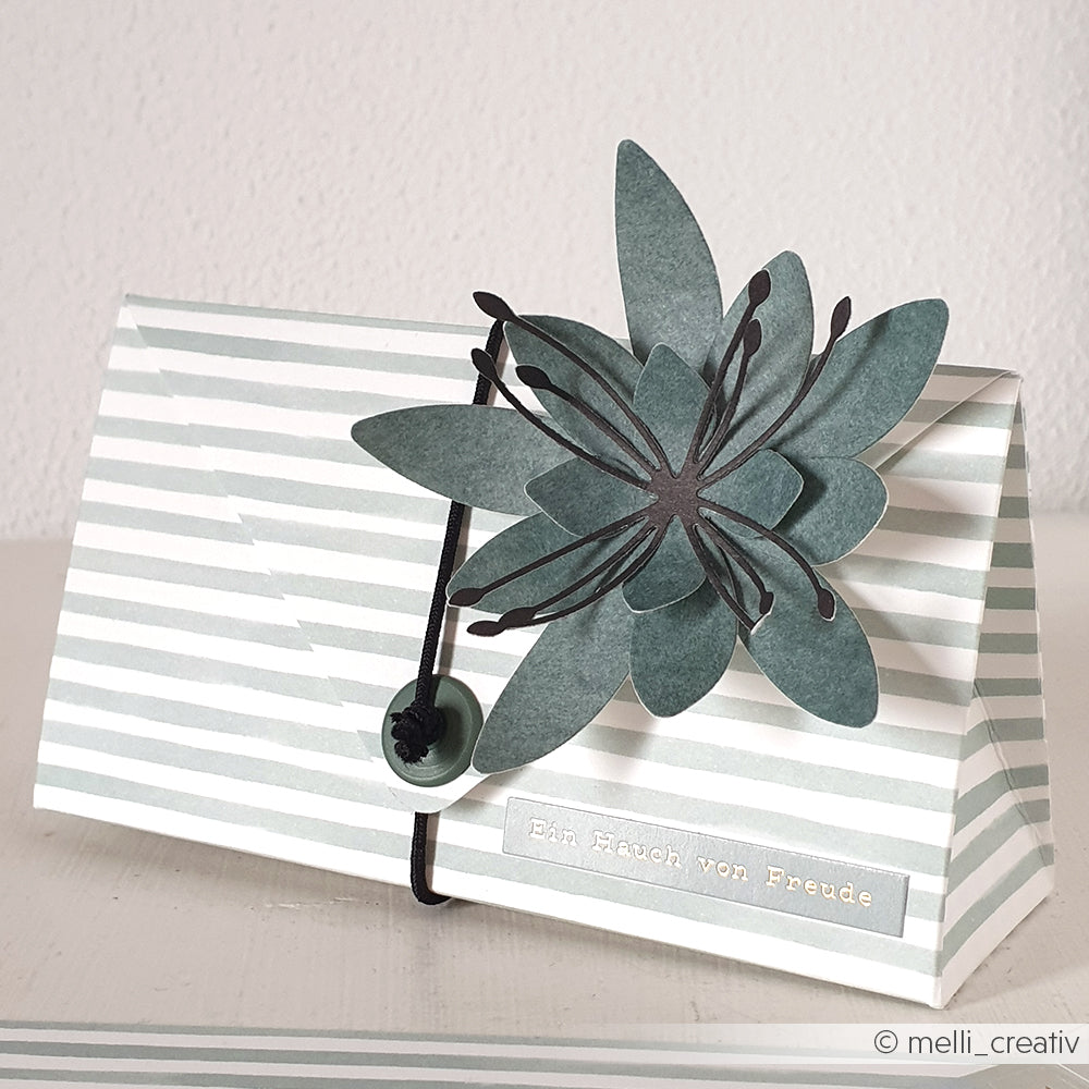 Gestreifte Papiergeschenkbox aus Alexandra Renke Designpapier, verziert mit einer großen Blume aus der Motivstanze 3D Sternblume und veredelt mit einem kleinen Etikett mit der Aufschrift "Ein Hauch von Freude".