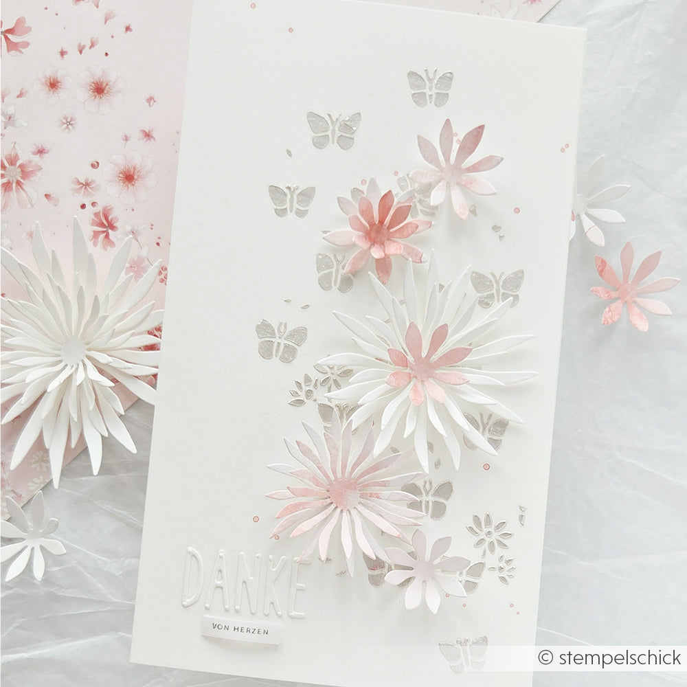 Weiße Karte von Alexandra Renke mit rosa-weißen 3D-Puschelblumen, mit dem Motivstanze DieCut-System ausgestanzten Schmetterlingen und der Prägung „DANKE“ unten links.