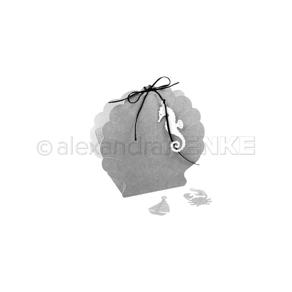 Die graue muschelförmige Geschenkbox von Alexandra Renke, die mit der Motivstanze Muschel Box hergestellt wurde, ist mit einem Seepferdchen-Anhänger und einer Schleife versehen, die neben einem Segelboot und Krabbenausschnitten zu sehen ist.
