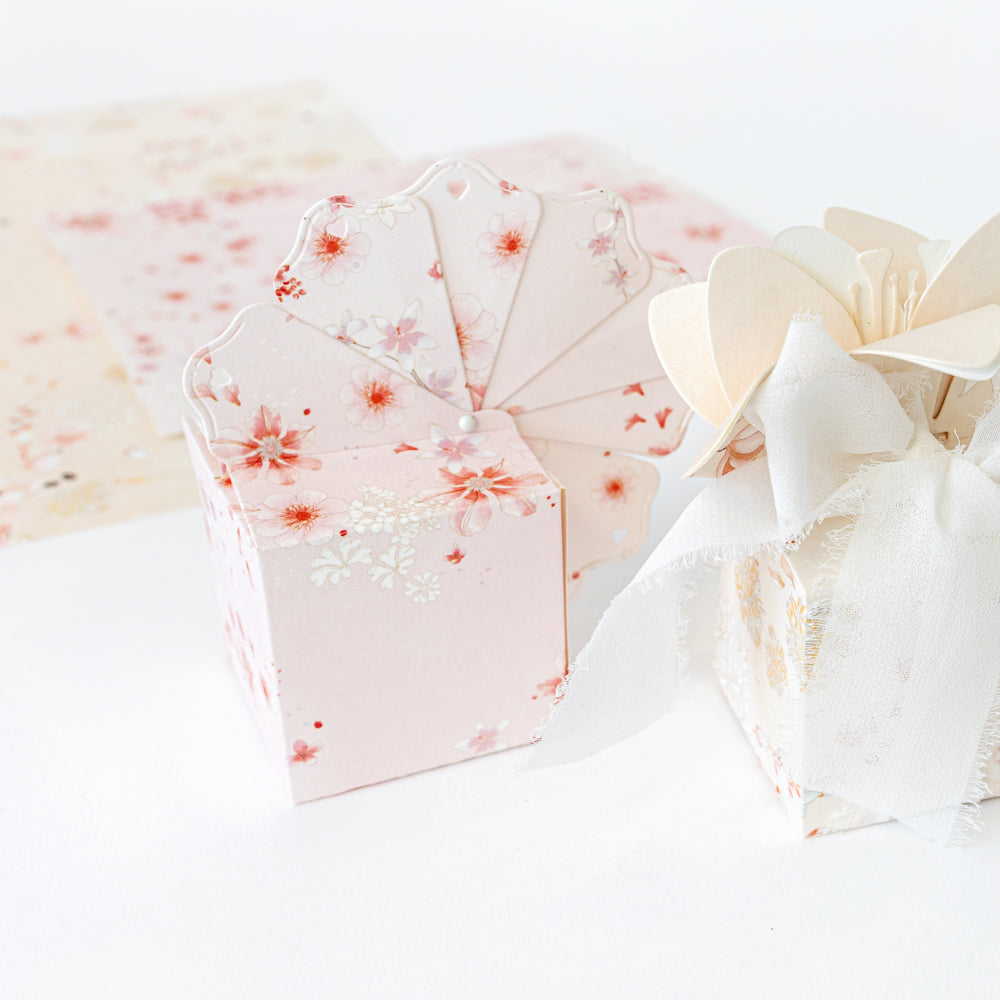 Pastellrosa Geschenkbox mit Blumenmotiv und passenden fächerförmigen Karten von Alexandra Renke, gefertigt aus hochwertigen Designpapieren unter Verwendung innovativer Stanzsysteme und verziert mit einem zarten weißen Stoffband.