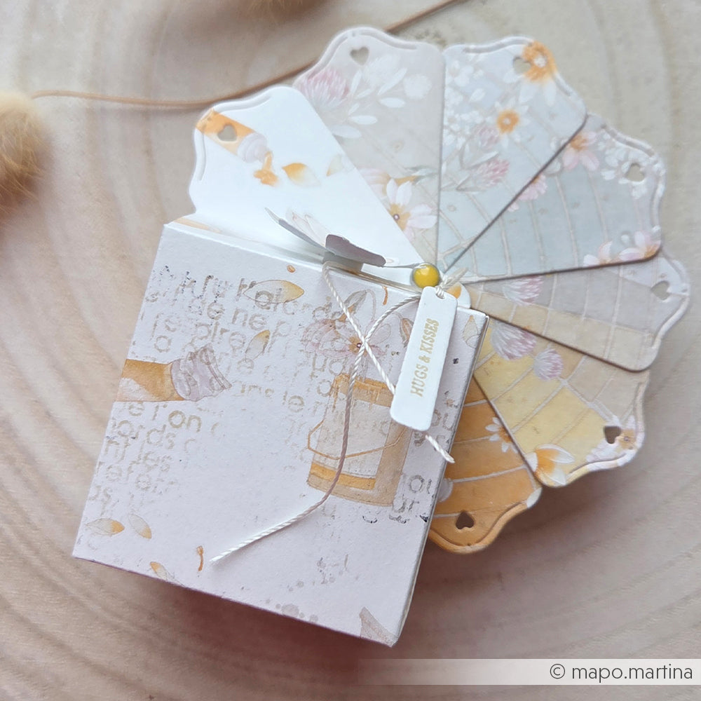 Ein handgefertigtes, pastellfarbenes Mini-Scrapbook mit fächerförmigen Seiten aus exquisiten Designpapieren von Alexandra Renke und den „Motivstanze Fächerbox“-Stanzsystemen. Abgerundet wird es durch ein bezauberndes Etikett mit der Aufschrift „PICCOLI RICORDI“.