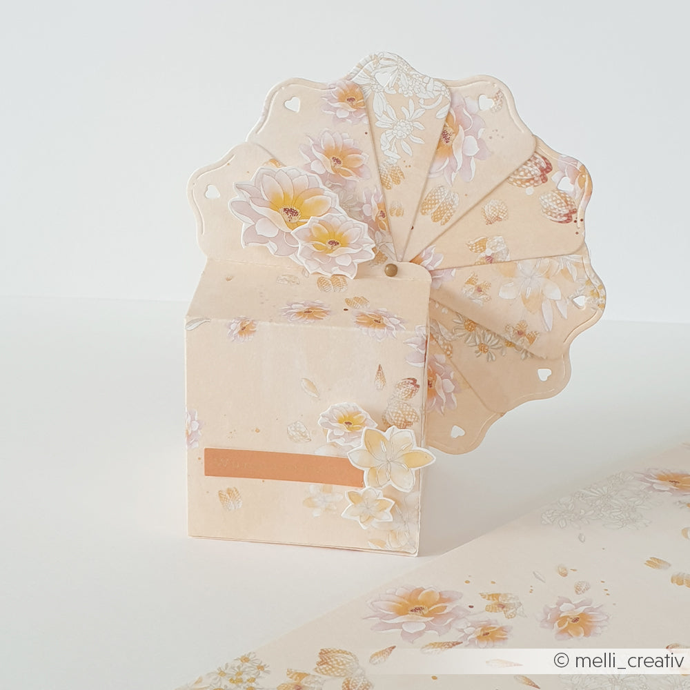 Beigefarbene, fächerförmige Karte mit zarten Blumenmotiven, gefertigt aus hochwertigen Designpapieren und mit der Motivstanze „Fächerbox“ von Alexandra Renke, die aufrecht auf einer passend gestalteten Unterlage steht.