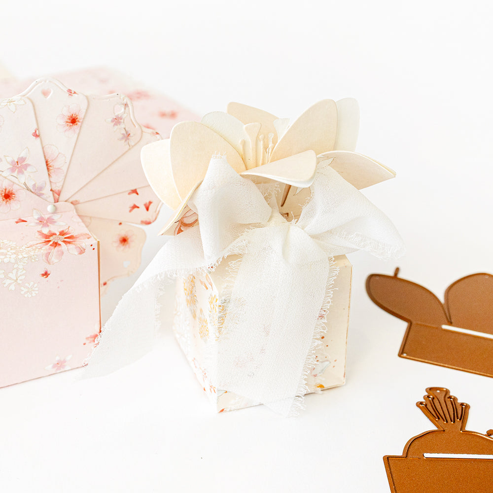 Geschenkbox mit Blumenmustern, verziert mit Papierblumen und einer weißen Schleife, daneben florale und braune Ausschnitte – die perfekte Inspiration für Ihr nächstes „Motivstanze Blumenbox“-Projekt mit den stilvollen Designpapieren von Alexandra Renke.
