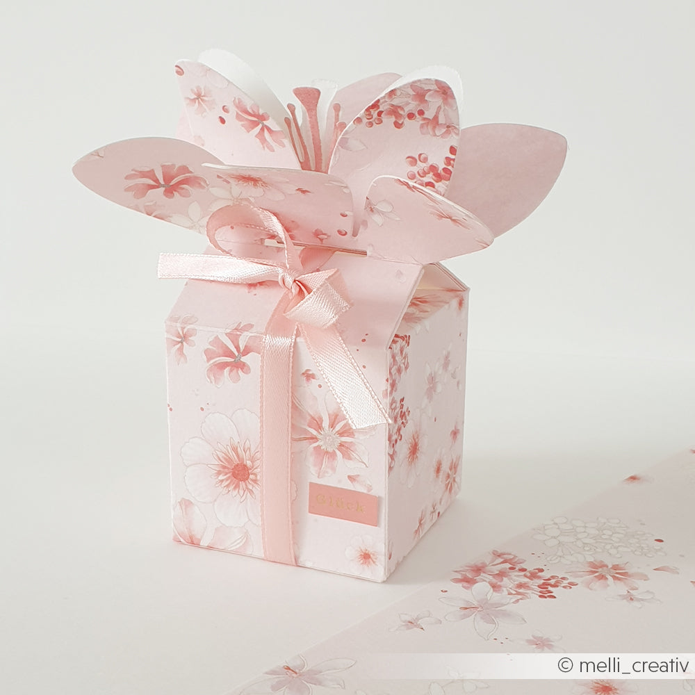 Rosa Geschenkbox mit Blumenmuster, blumenförmigem Deckel und Schleife, gefertigt mit der „Motivstanze Blumenbox“ von Alexandra Renke und eleganten Designpapieren von Alexandra Renke, auf weißem Untergrund platziert.