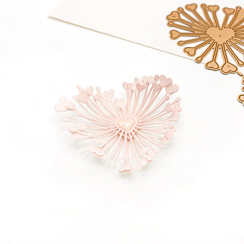 Ein rosa, herzförmiger Papierschnitt, der mit der Alexandra Renke Motivstanze „3D Herzchen Blume“ mit strahlenförmigen Linien gestaltet wurde, liegt neben einer goldenen Variante auf einem weißen Untergrund – ideal, um Ihren Designpapieren einen besonderen Charme zu verleihen oder in Kombination mit verschiedenen Stanzsystemen zu verwenden.