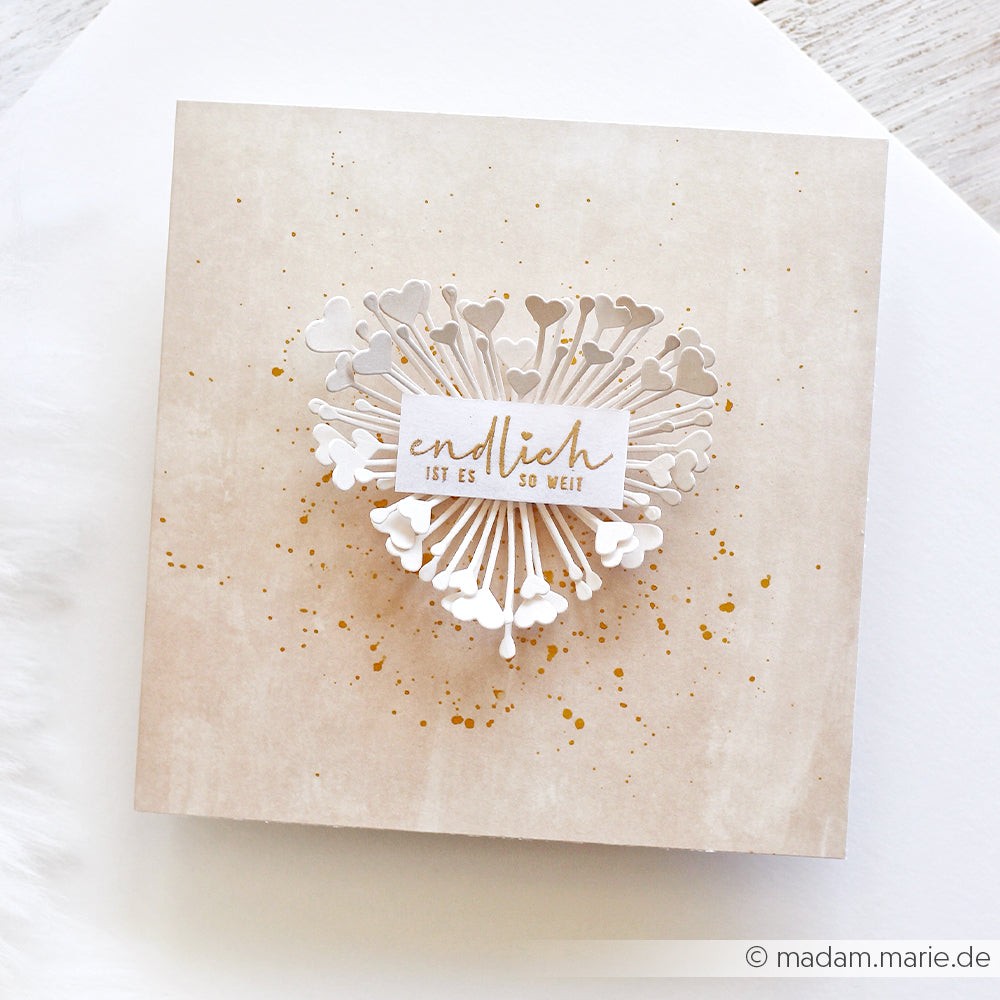 Quadratische Karte, verziert mit herzförmigen Papierausschnitten, die mit der „Motivstanze 3D Herzchen Blume“ von Alexandra Renke ausgestanzt wurden, sowie einem eleganten goldenen Schriftzug „endlich ist es so weit“ oben auf der Karte.