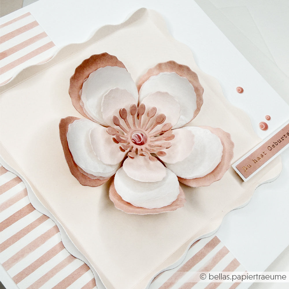 Handgefertigte Karte mit einer wunderschönen 3D-Blume aus rosa und weißem Papier, die mit der „Motivstanze 3D Wolkenrose“ von Alexandra Renke und hochwertigen Designpapieren gestaltet wurde. Das Design wird durch gestreifte Akzente und ein kleines „Happy Birthday“-Anhängchen ergänzt und unterstreicht die Präzision moderner Stanzsysteme – für eine wahrhaft einzigartige Note.