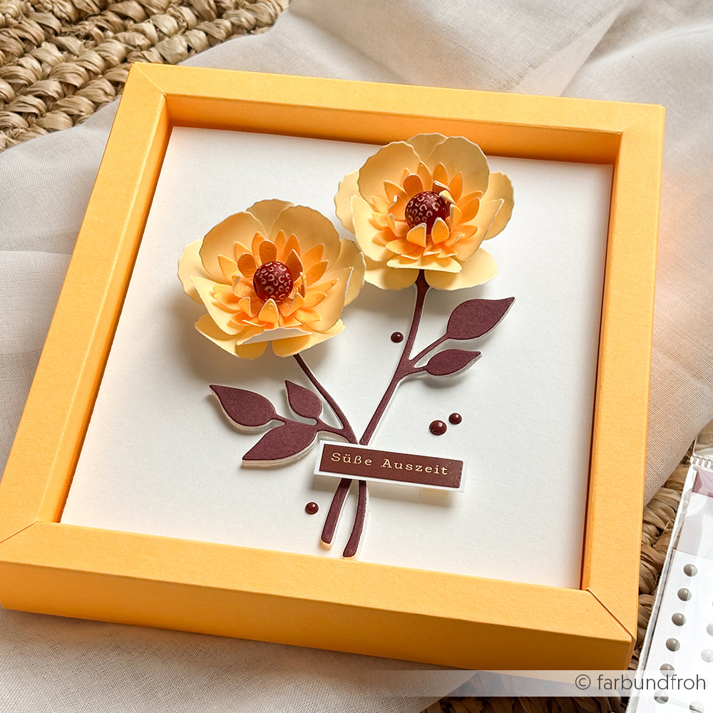 Gerahmtes 3D-Papierkunstwerk mit zwei gelben Blumen mit braunen Stielen und Blättern, gefertigt mit der Motivstanze „3D Wolkenrose“ und hochwertigen Designpapieren, mit einem bezaubernden „Süße Auszeit“-Etikett darunter.