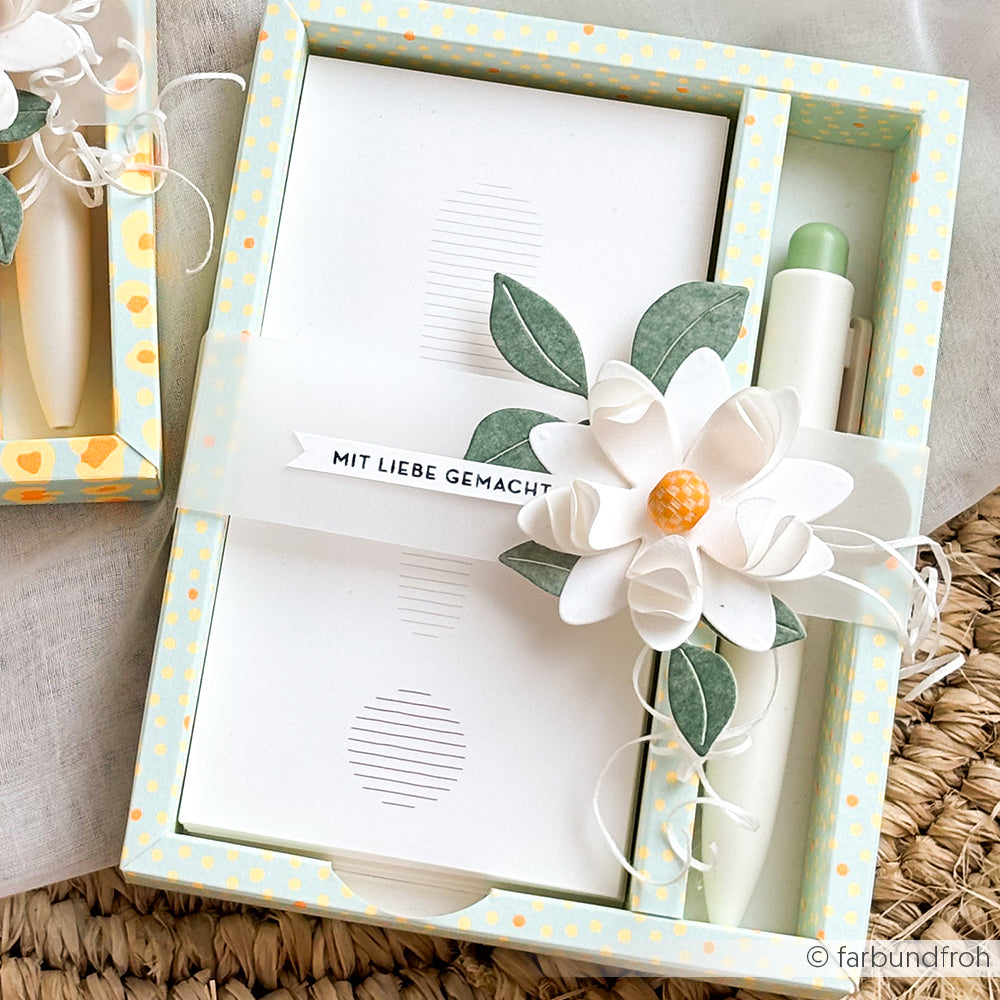 Geschenkbox mit Notizblock, Stift und weißer Papierblume, verpackt mit einem Etikett mit der Aufschrift „Mit Liebe gemacht“. Die zarte Blume ist mit Akzenten verziert, die mit der 3D-Motivstanze „Sternensee Rose“ gestaltet wurden, und wird durch elegante Designpapiere ergänzt, die ihr eine edle Note verleihen.