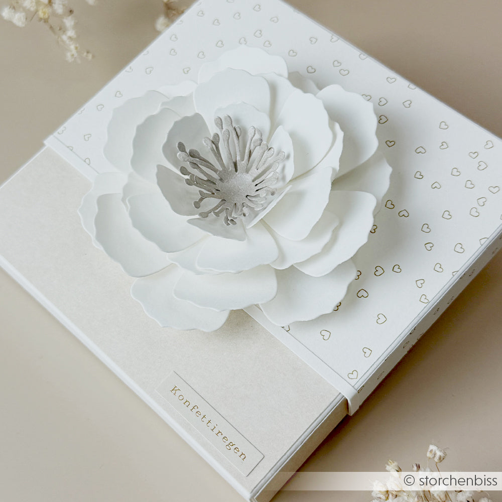 Weiße Geschenkbox von Alexandra Renke mit einer großen, detailreichen 3D-Pfingstmondblume aus Designpapier und kleinen Herzmustern auf dem Deckel – ein Unikat, das sich perfekt für besondere Anlässe eignet.