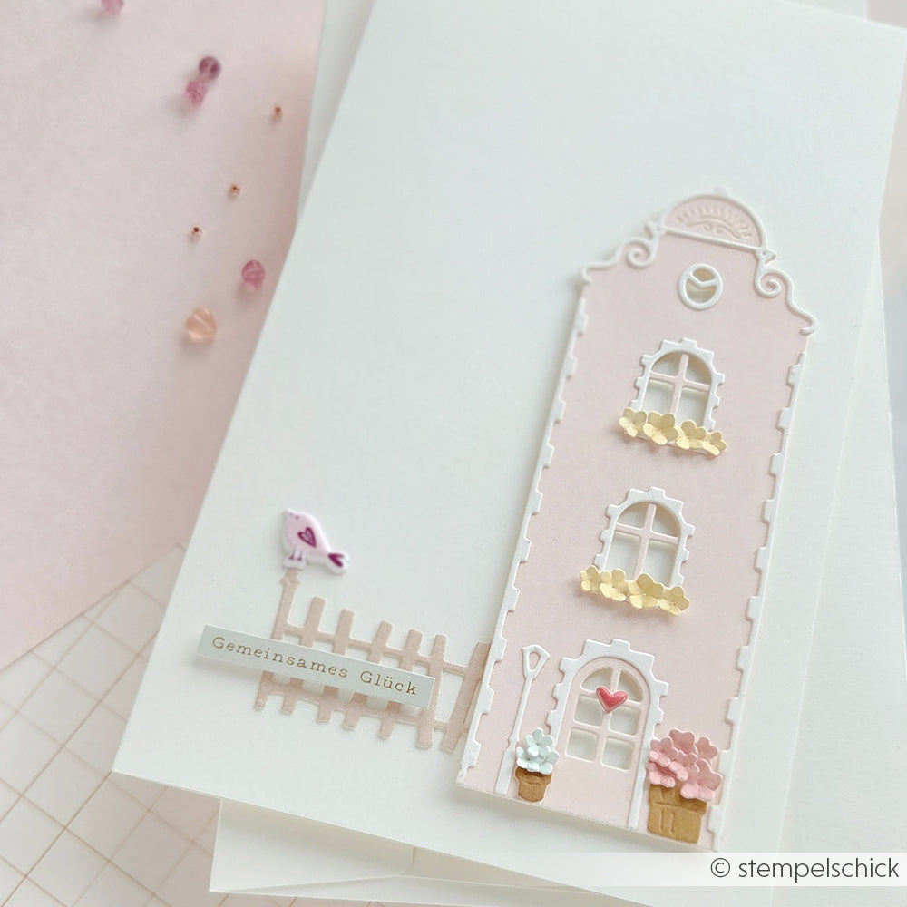 Handgefertigte Karte mit einem rosa Haus, Blumen, einem Lattenzaun und dem deutschen Text „Gemeinsames Glück“, hergestellt aus hochwertigen Designpapieren für zusätzlichen Charme.
