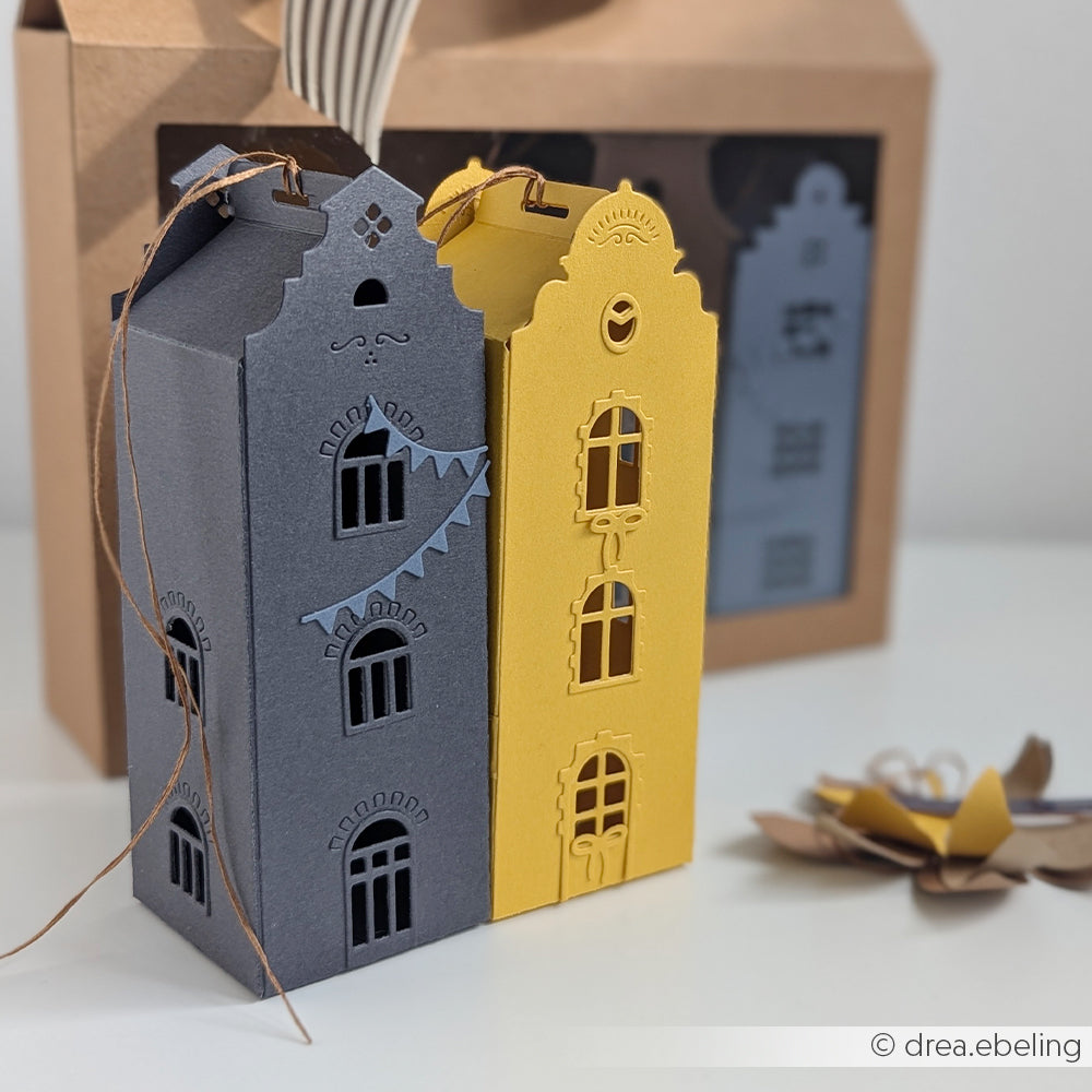 Geschenkboxen aus Papier in Form von grauen und gelben Häusern, gefertigt mit der Motivstanze „Häuserbox“ und stabilem Designpapier (200 g), sind mit dekorativen Fenstern und Schnurgriffen versehen und sorgen so für eine bezaubernde Präsentation.
