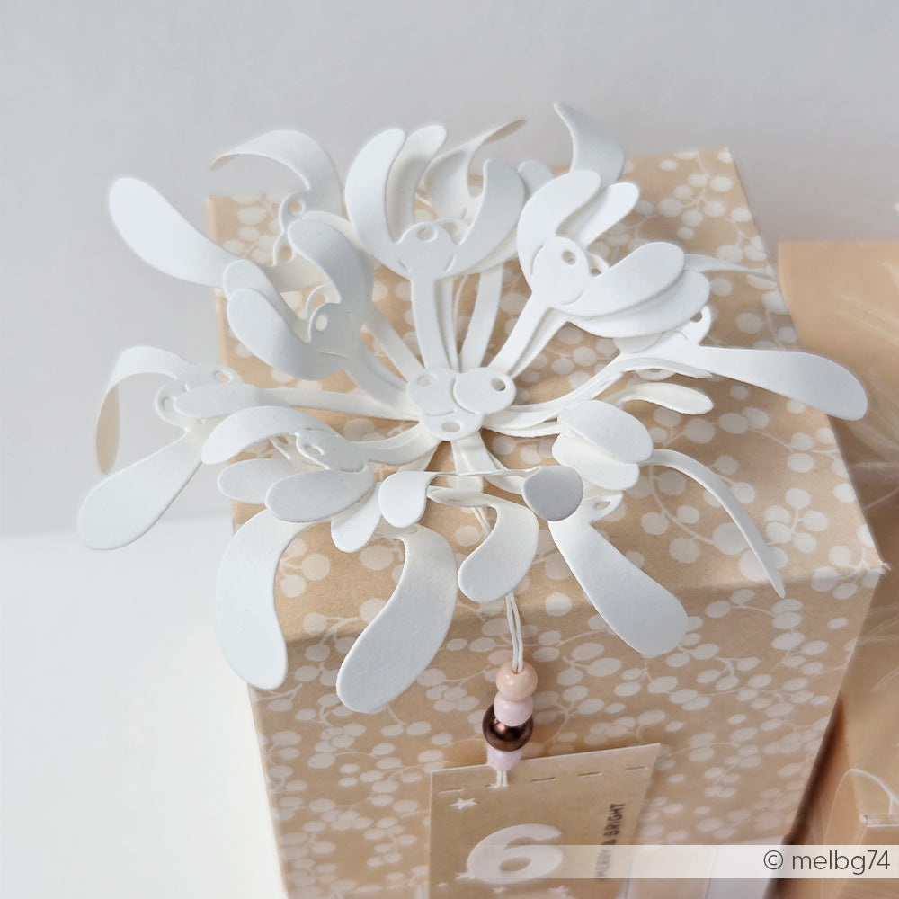 3D-Mistelzweig-Anhänger aus Designpapier, an einer Geschenkbox mit einem nummerierten Anhänger befestigt.