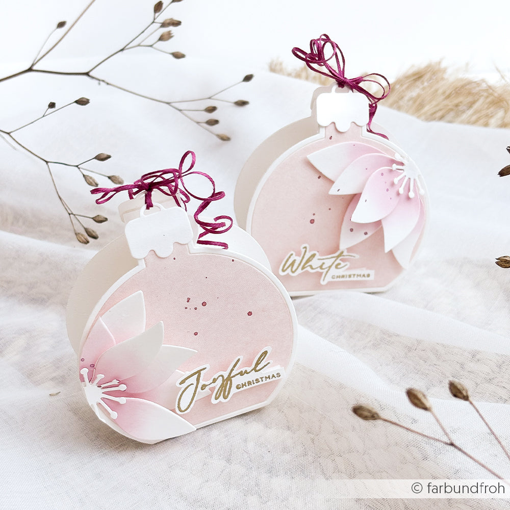 Zwei Geschenkboxen in Form von Weihnachtsschmuck, verziert mit 3D-Papierblumen in Form von Weihnachtssternen.