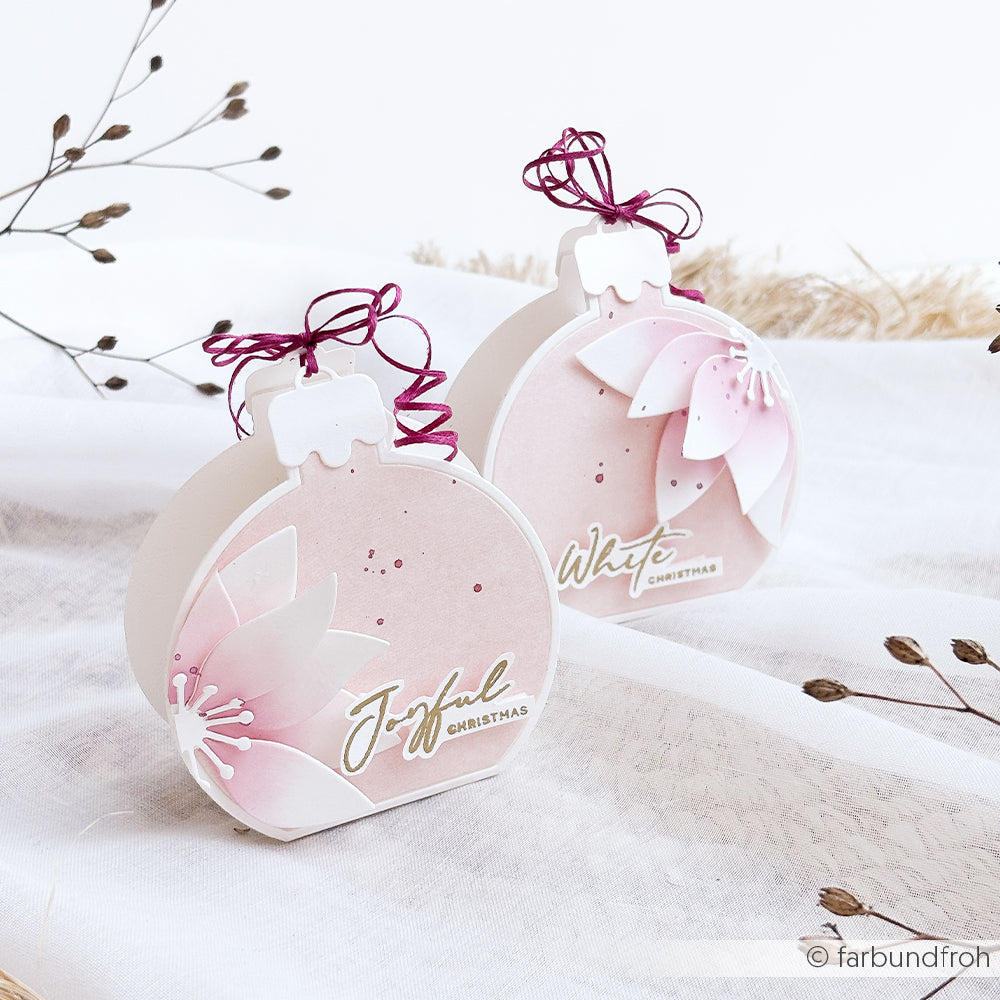 Zwei handgefertigte Motivstanze-Weihnachtskugel-Schmuckstücke mit den Aufschriften Joyful und White Christmas.