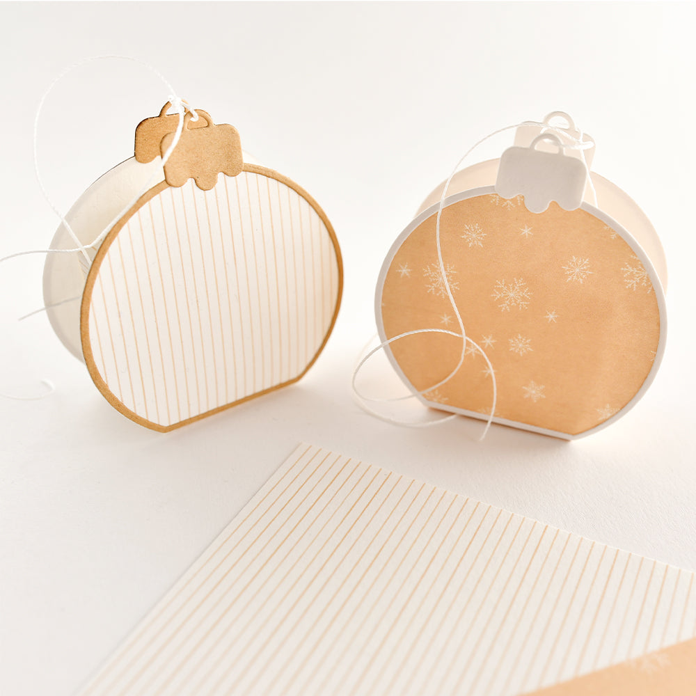 Zwei geschenkverpackungen in Form von Weihnachtskugeln, gestaltet mit Designpapieren und Aufhängeschnüren, hergestellt mit einer Motivstanze „Weihnachtskugel“.