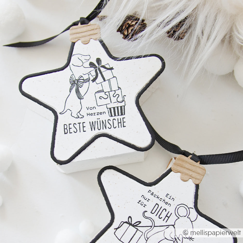 Zwei sternförmige Motivstanze-Weihnachtskugel-Anhänger mit einem Hund und einer Maus, die Geschenke tragen.